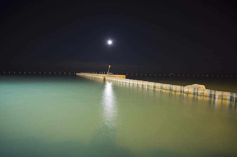 moon over green water and jetty